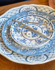 stacked plates from a disassembled blue and white 3-tier tray, held in two hands with silver hardware on top
