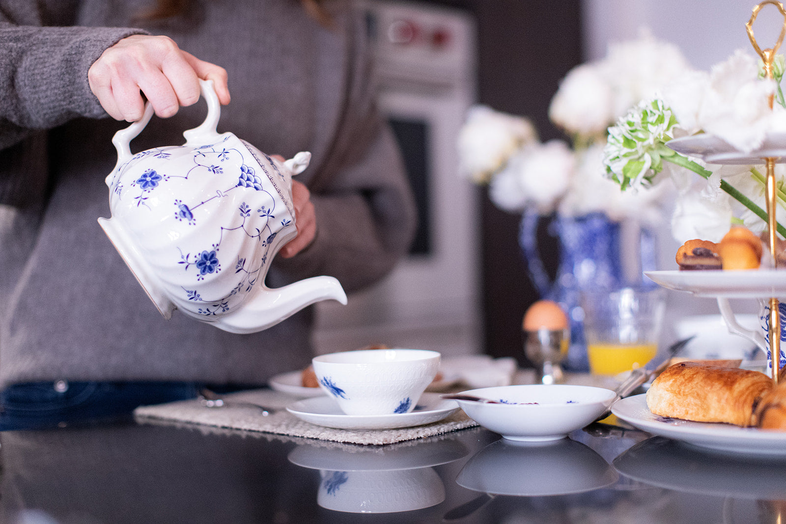 Blue and white teapot being poured into antique Rosenthal fine bone china tea cup. 3-Tier Tray serving croissants and pastries and flowers arrangement in a calico staffordshire teapot 