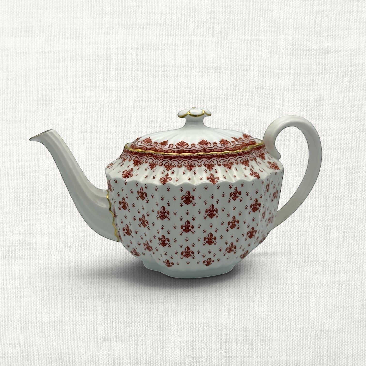 A white porcelain teapot with a red floral pattern and gold trim