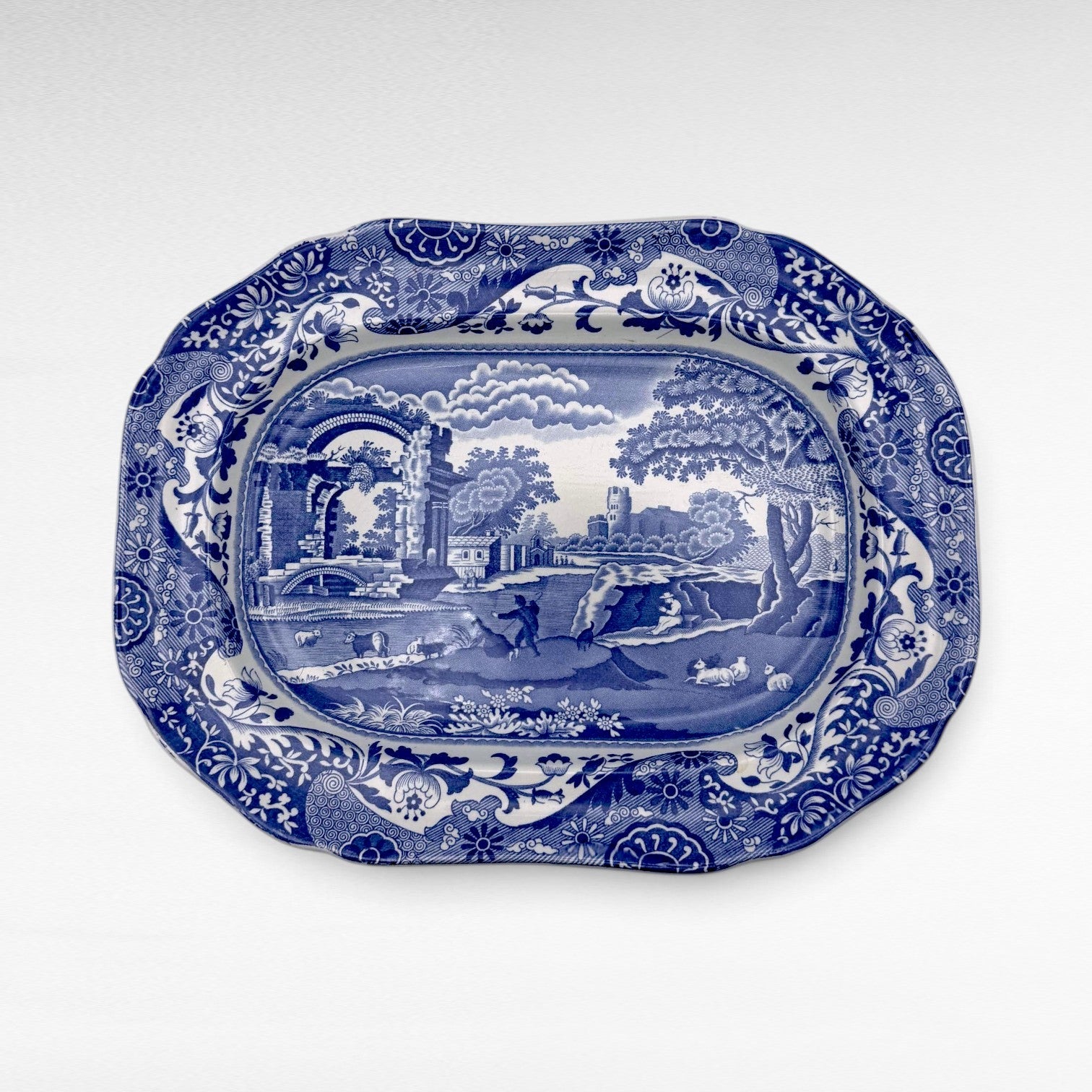 A blue and white vintage serving platter with a detailed landscape scene in the center and ornate floral borders