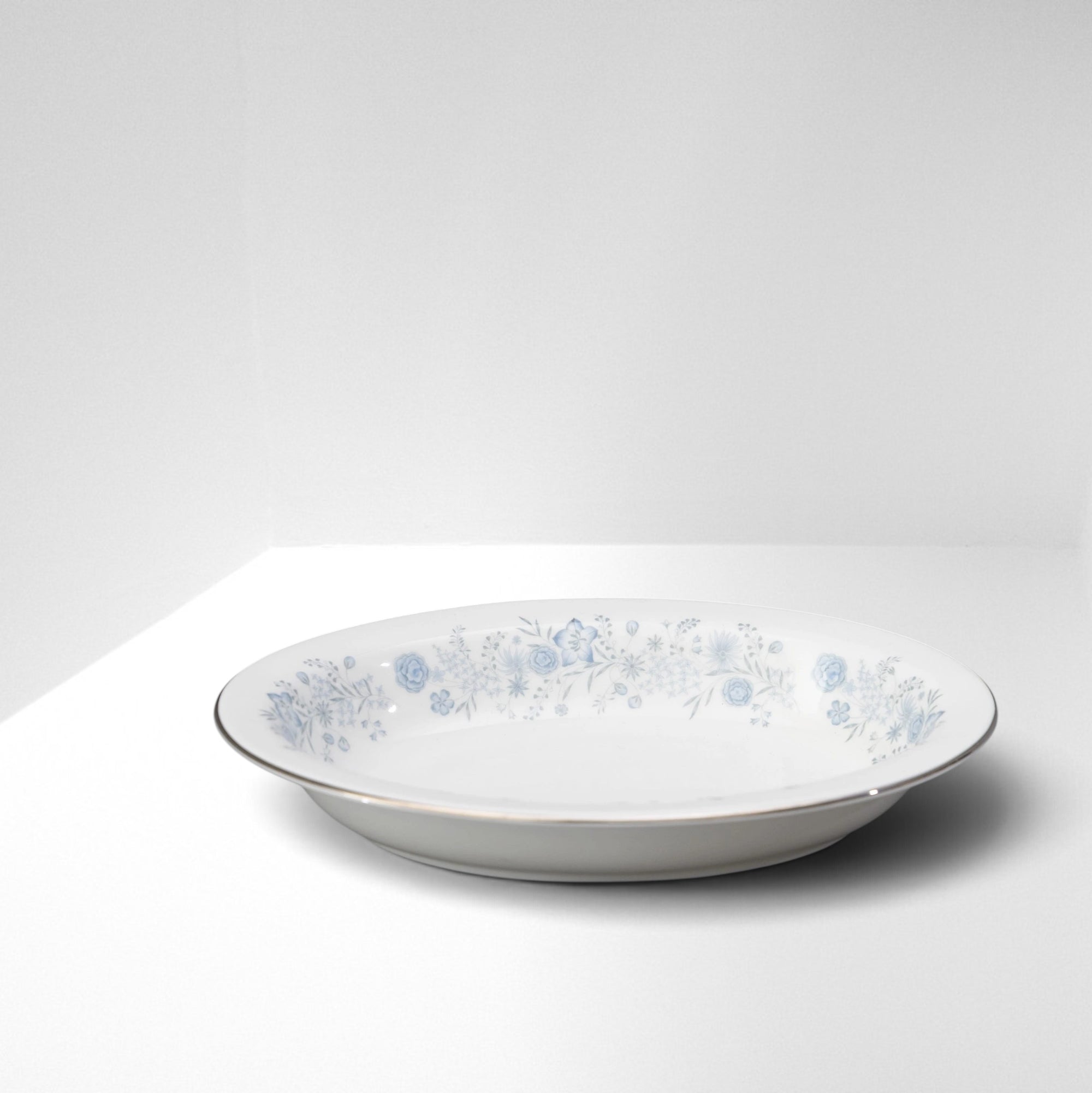 The Brooklyn Teacup oval serving bowl in white porcelain with a delicate blue floral pattern and silver rim.