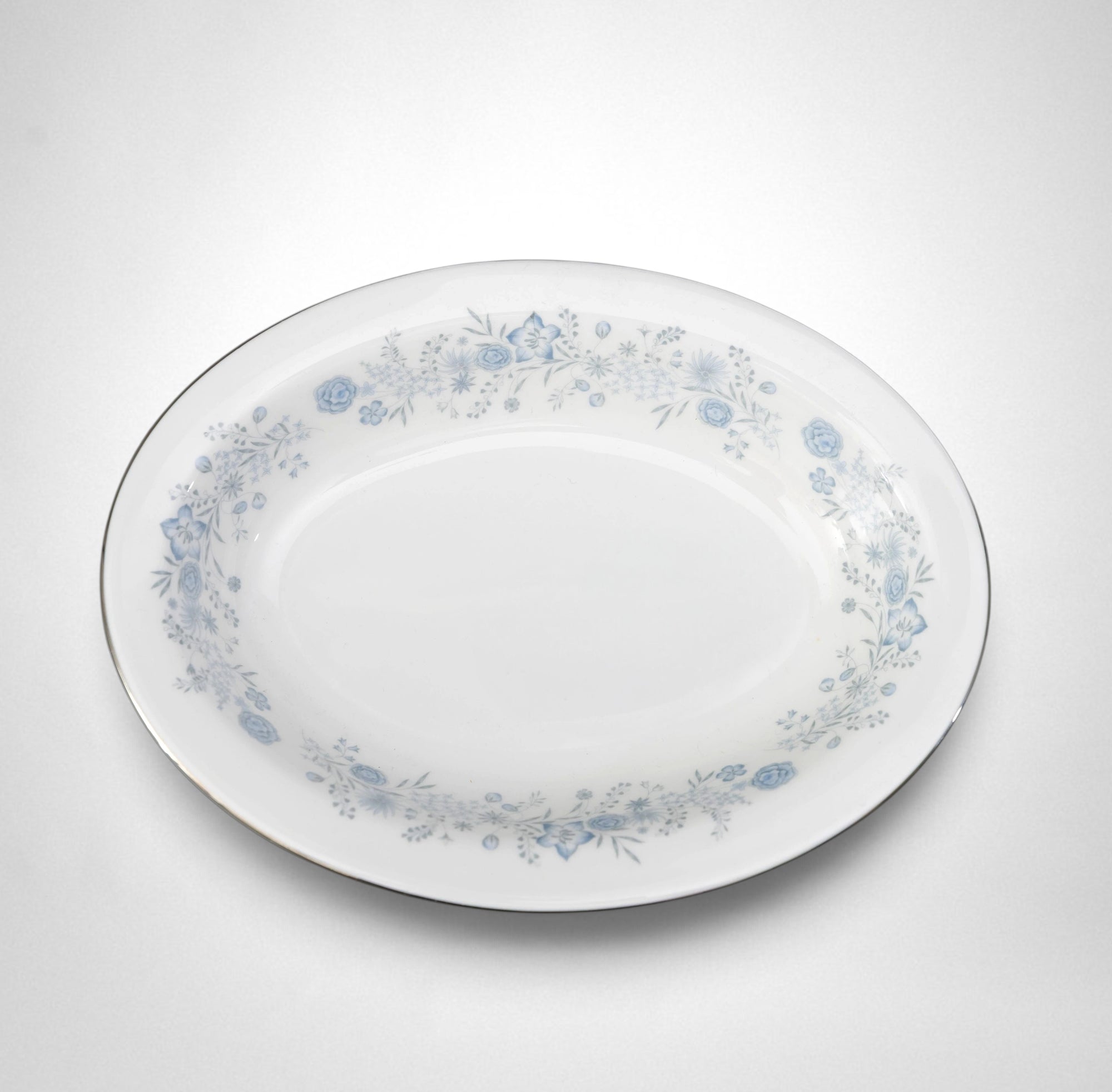 The Brooklyn Teacup oval serving bowl in white porcelain with a delicate blue floral pattern and silver rim.