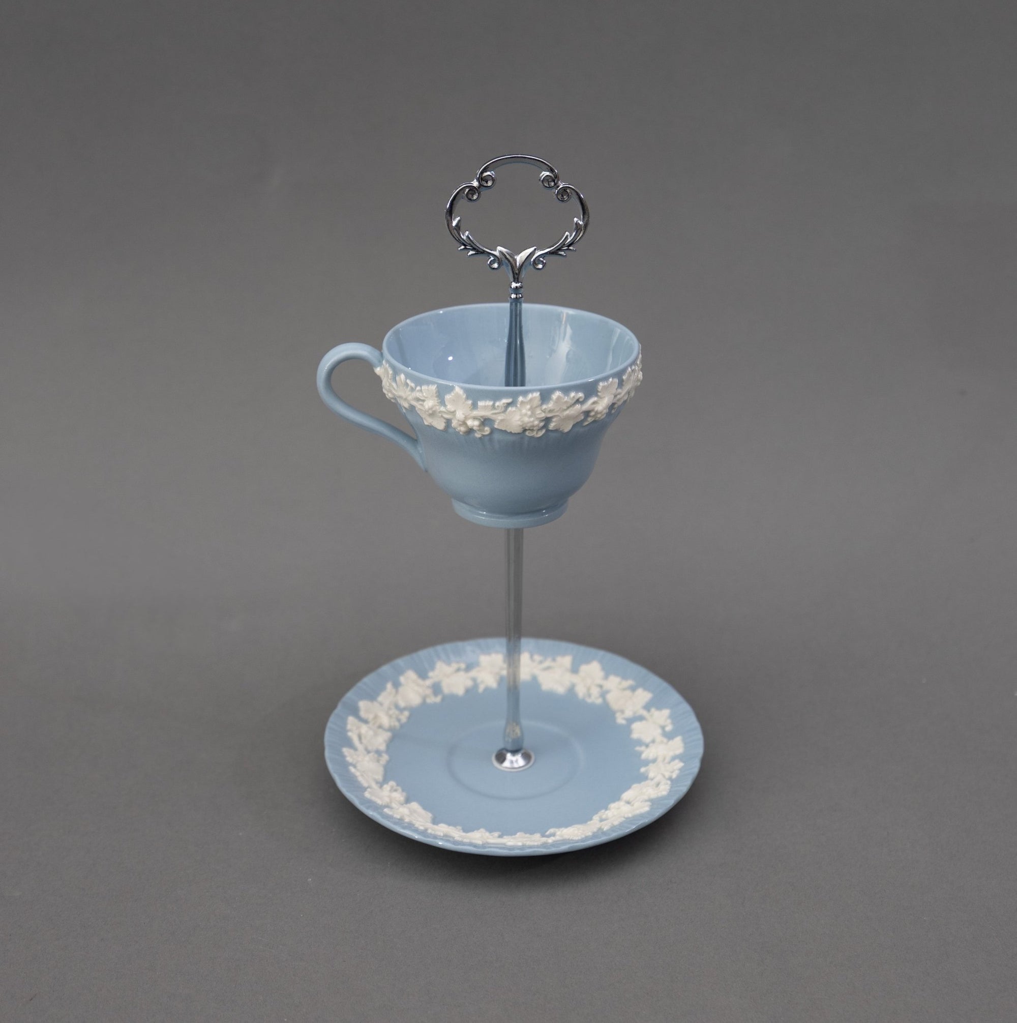 Decorative Wedgwood Queensware blue cup and saucer with ivy lace detailing on a gray background with silver hardware